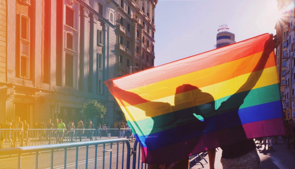 Schwules Paar hinter einer Regenbogenflagge - Bild: deivitt via Twenty20