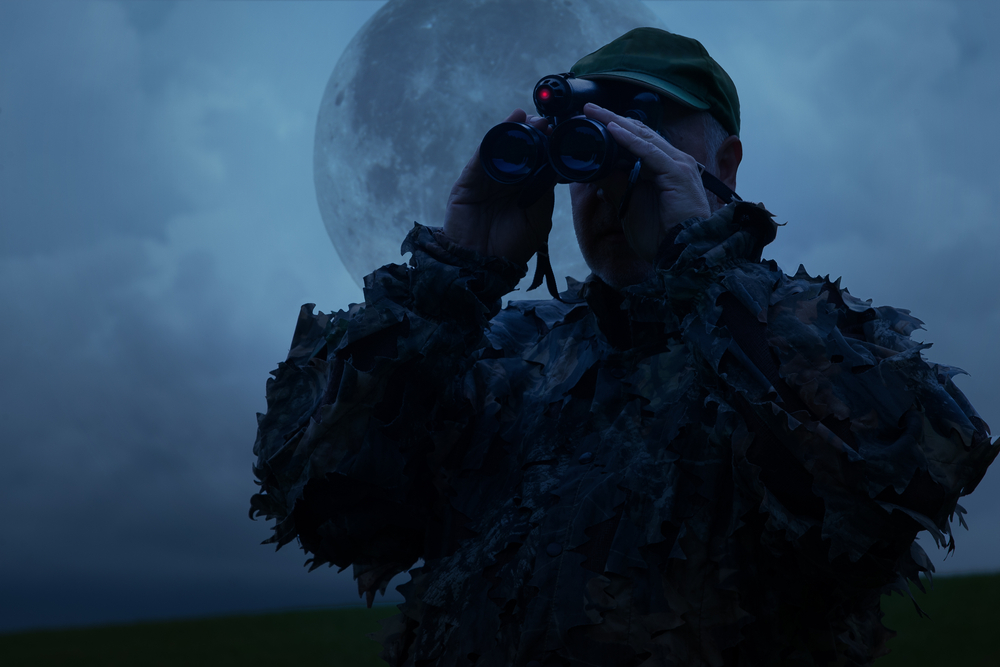 Jäger beobachtet sein Jagdgebiet mit einem Nachtsichtgerät unter Vollmond. - Bild: Shutterstock/Edgar G Biehle