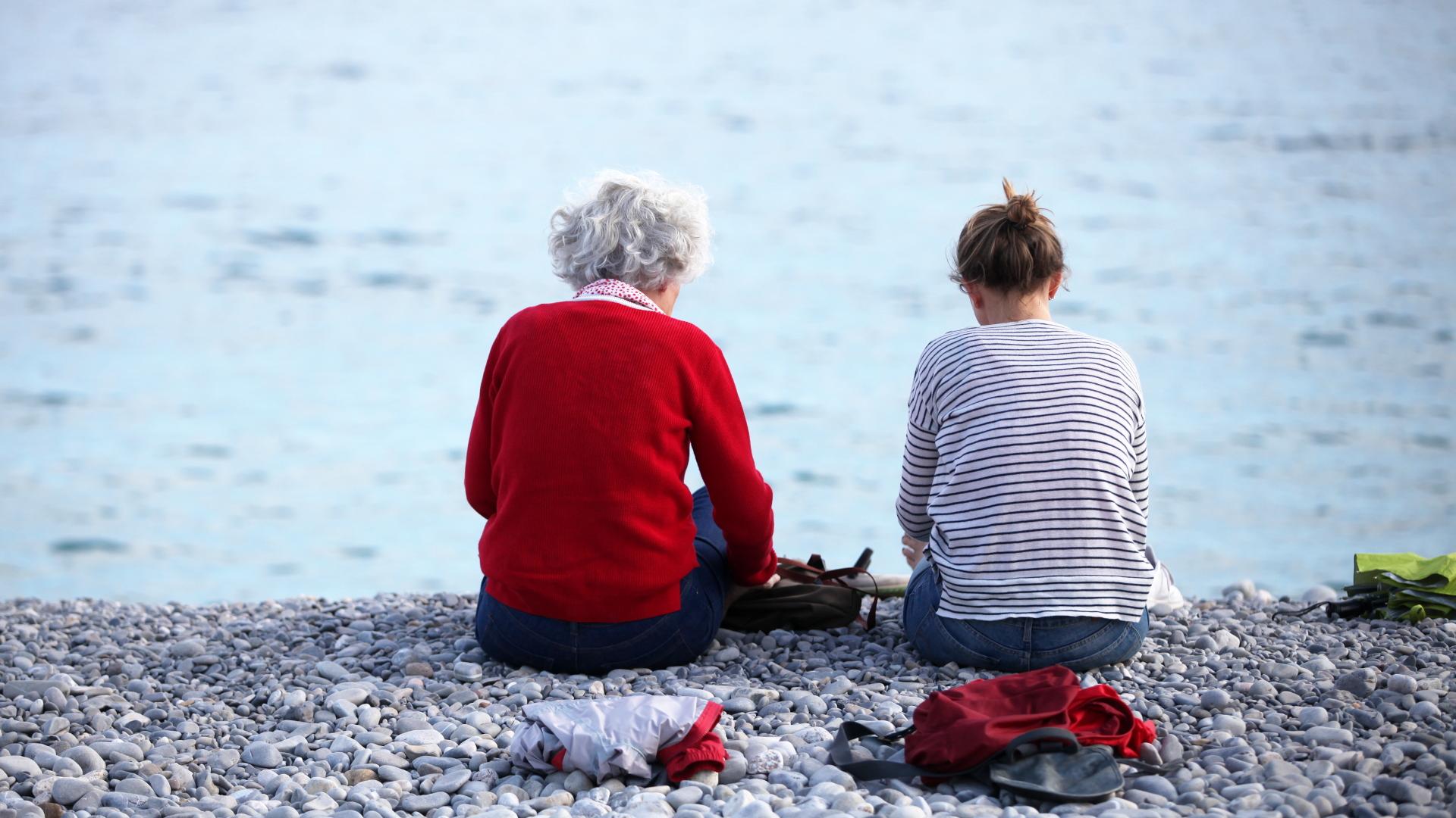 Alte und junge Frau sitzen am Strand (über dts Nachrichtenagentur)